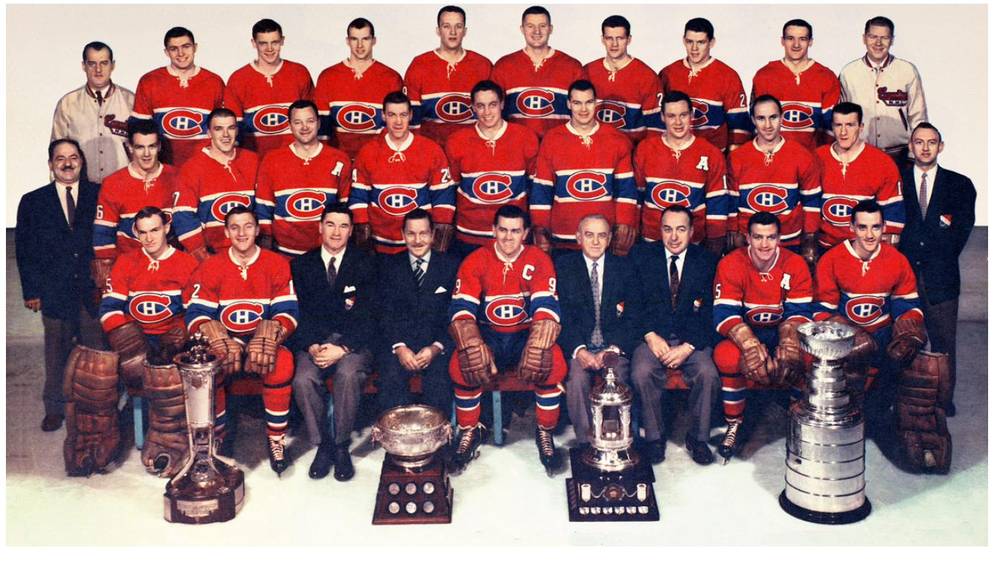 A formal team photograph of the Montreal Canadiens in red sweaters, seated in rows behind several trophies including the Stanley Cup.