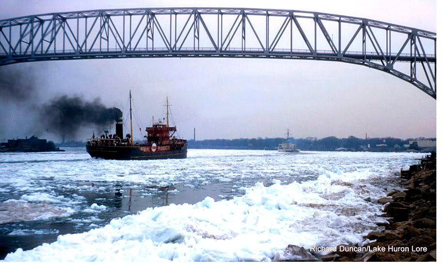A tanker working through heavy ice beneath a large steel arch bridge.
