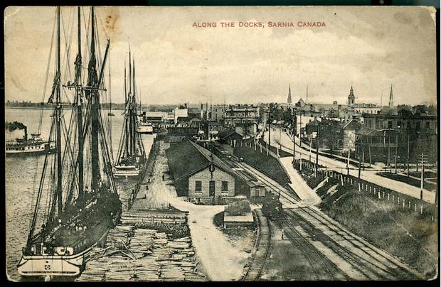 Masted schooners along a waterfront with railway tracks.