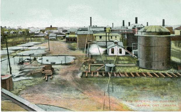 Low industrial sheds and a large riveted tank on bare ground.