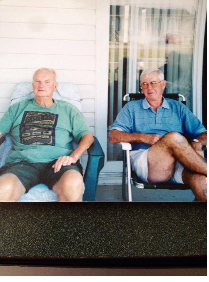 Two older men sitting in lawn chairs on a porch in summer clothes.
