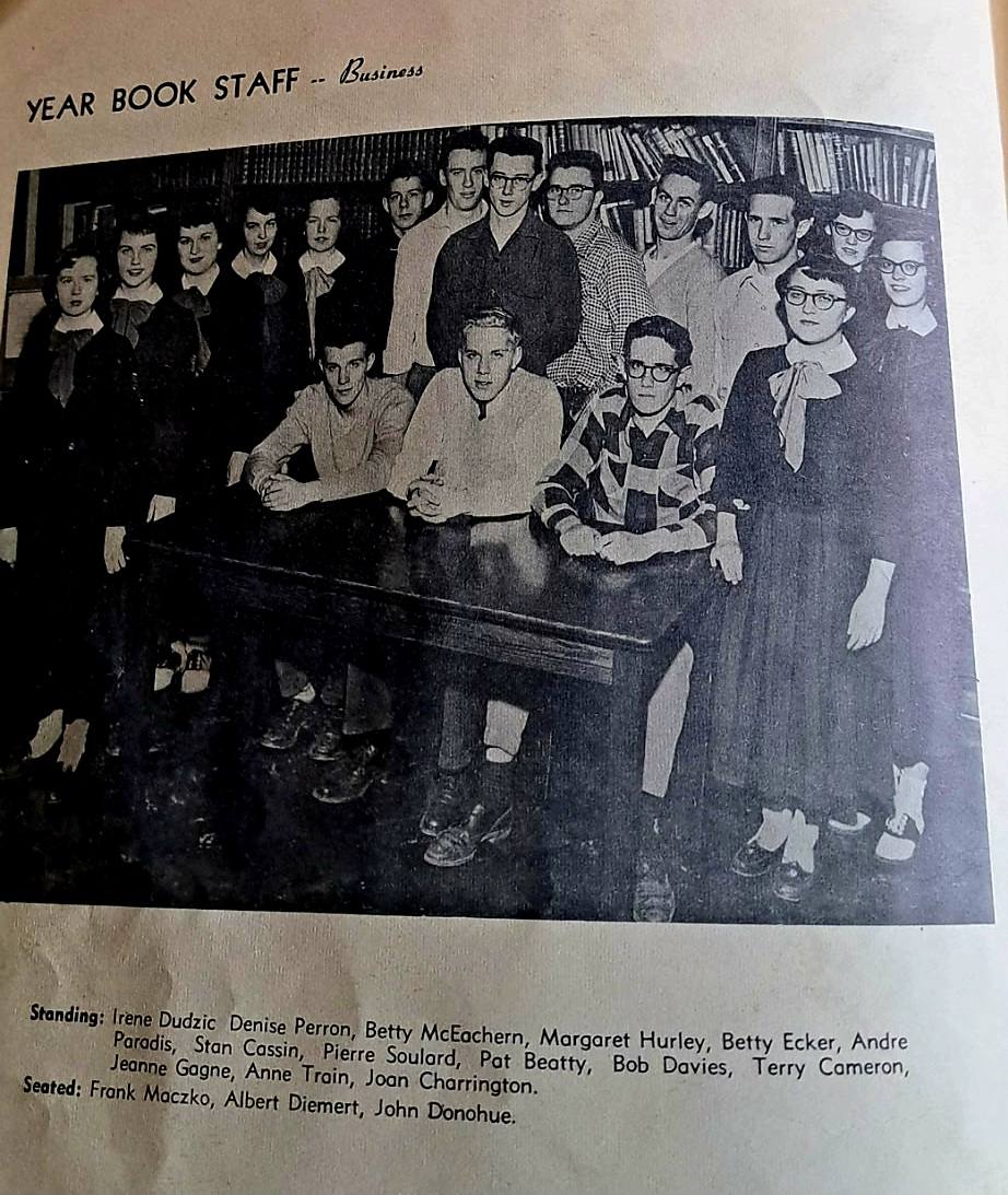 Sixteen teenagers in 1950s clothes posed around a library table, captioned Year Book Staff, Business.